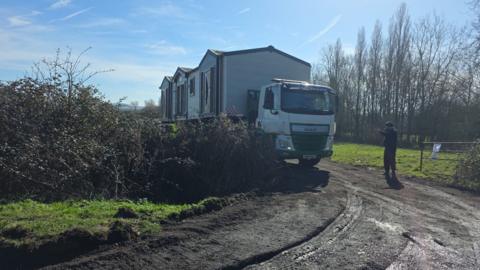 A truck carrying a mobile home drives onto a field.