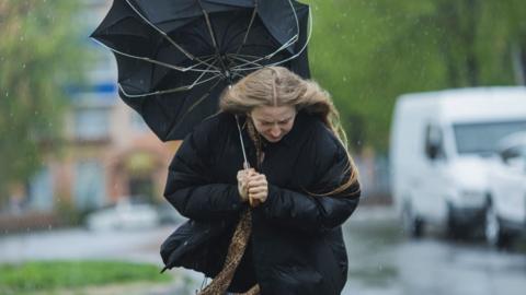 A woman struggling against wind and rain with an umbrella that has bent inside out