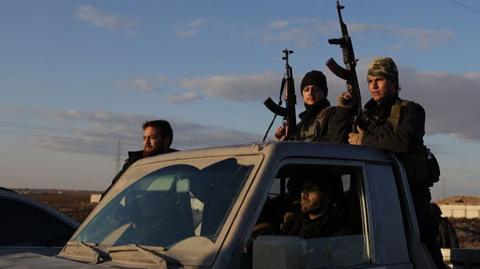 Syrian government forces hold rifles while riding on a pick-up truck on the road to Raqqa, Syria (19 January 2026)
