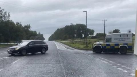 Road closure with police tape and several police vehicles in frame