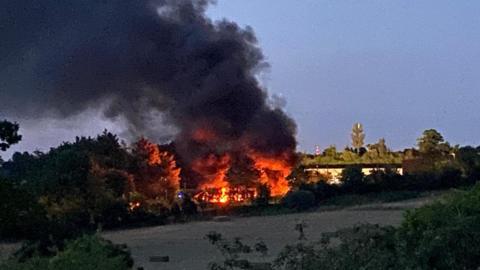 The skip lorry site in College Road, Epsom on fire, with thick black smoke and flames filling the air.