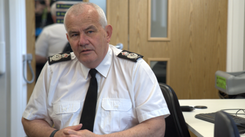 Simon Blatchly, in police uniform, sitting at a desk