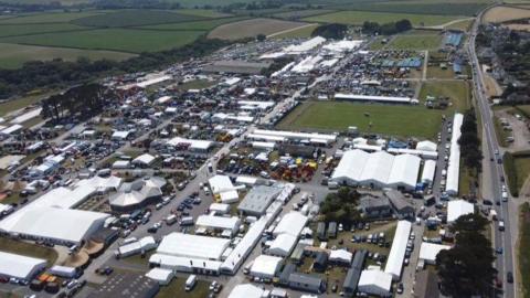 An aerial view of the Royal Cornwall Showground in Wadebridge in 2024. There are lots of white marquees and tents around the site, with cars and people dotted around as well.