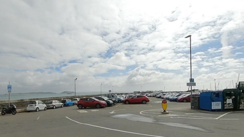 Cars parked at a car park in Guernsey. Water is in the background. 