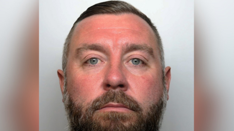 Police mugshot of a man with blue eyes and a short beard