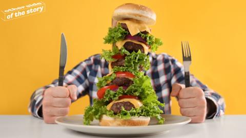 Man with face hidden behind highly-stacked burger