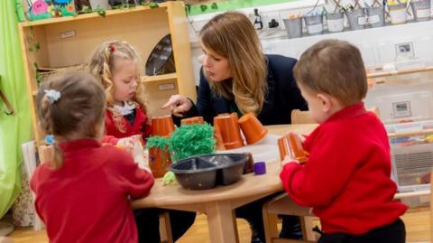 North East Mayor Kim McGuinness primary School pupils at their breakfast club. They are sitting around a small table playing with plastic plant pots. 