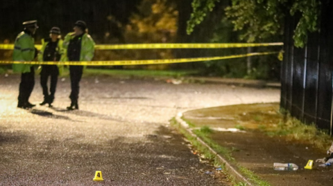 Police stand close to a crime scene cordon on a street