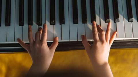 A child's hands play on white and black piano keys