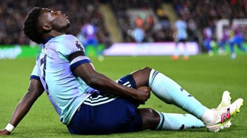 Arsenal's Bukayo Saka holds the back of his leg as he sits on the field after suffering an injury against Crystal Palace