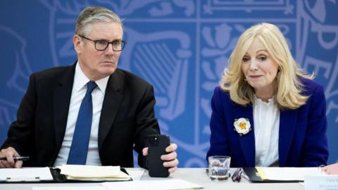 Sir Keir Starmer sits alongside Tracy Brabin at a desk, with a blue background. 