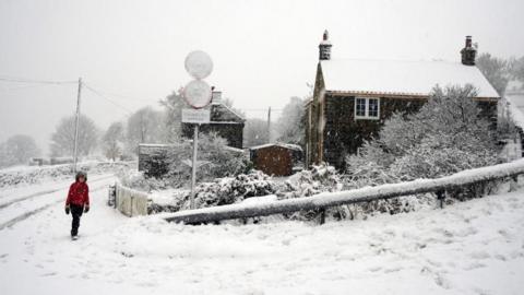 A boy wearing a red coat walks along a snow-covered street.
