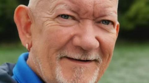 William Chapman, 58, who is bald, with a white goatee and wears a gold ring in his right ear, smiles at the camera.