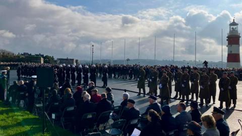 Military personnel and veterans taking part in the Remembrance service on Plymouth Hoe. The red and white lighthouse is visible on the right hand side