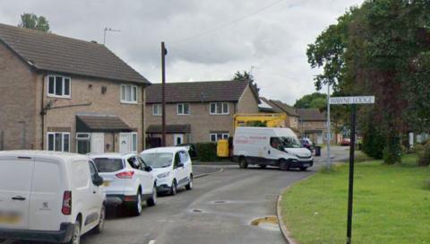 Vehicles parked outside houses on a street with a road sign labelled Wawne Lodge