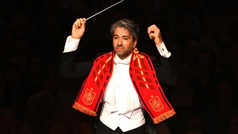 Orchestra conductor wearing a red football scarf