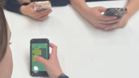 A picture of schoolchildren on their mobile phones, sat surrounding a white table.