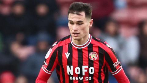 Evan Weir in a red and white Walsall shirt in action on the pitch