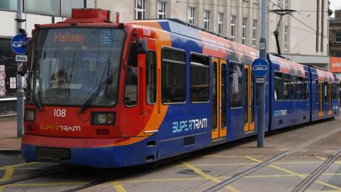 A blue and red tram. The doors are closed and the electronic sign at the front reads, 'Halfway'.