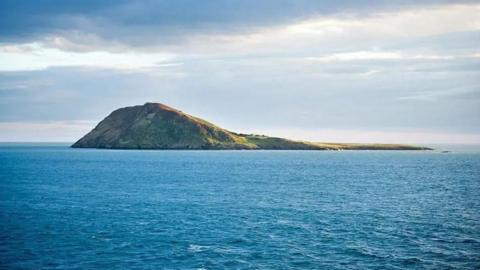 A rocky islet sits in the middle of the sea.