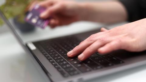 A person typing on a laptop with a credit card held in their right hand.