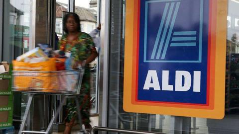 A woman pushing a trolley exits an Aldi supermarket