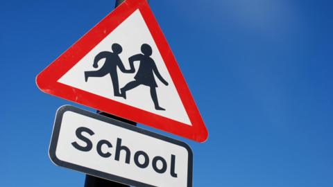 A UK warning triangle road sign, indicating that a school is nearby.