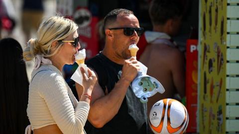 A man and woman wearing sunglasses each eat an ice cream at Bournemouth Beach. 