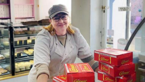 Woman poses behind stacks of Caramac boxes.