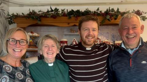 From left to right is a Lorna Brown with short blonde hair and is wearing a patterned top, Reverend Hawthorne-Steele with short hair and a green shirt with clerical collar, Reverend Chris Bennett with brown hair and beard wearing a striped shirt and clerical collar and a man with short grey hair wearing a zip-up fleece.