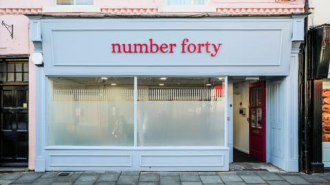 The exterior of 'number forty' welfare hub on a Darlington street. It is painted pale blue, with a red door to the right of the shop window standing open to the public.