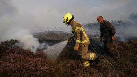 A firefighter helps combat a fire on heathland alongside the A171 road on August 14, 2025 in Fylingdales.
