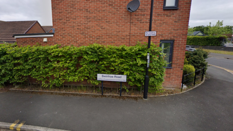 Side of brick new-build house with a street light and road sign in front. The road sign read Swinhoe Road. 