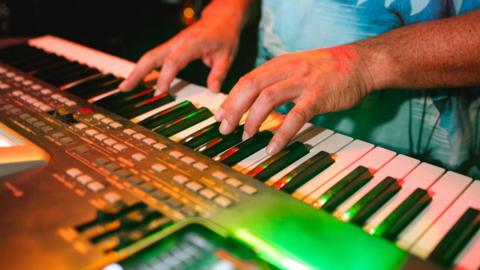 A man's hands are playing a keyboard in a music studio