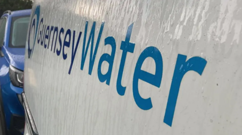 A sign on the side of a white vehicle. It says 'Guernsey Water' in blue writing.