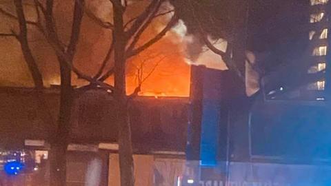 An image of a sky glowing orange due to fire. A high rise block of flats can be seen to the right and trees in the foreground.