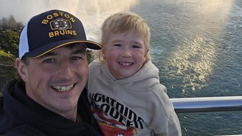 Liam Carr with his three-year-old son. Liam is wearing a baseball cap.