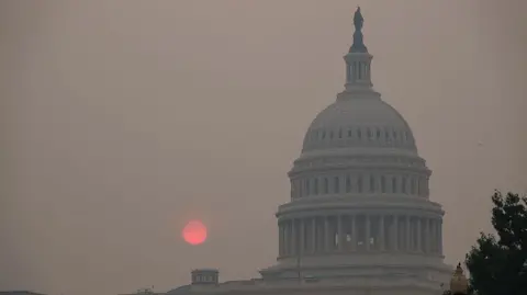 Capitol building at dawn surrounded by haze with an orange sun rising