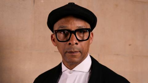 Jay Blades wearing a black cap, black jacket and white shirt