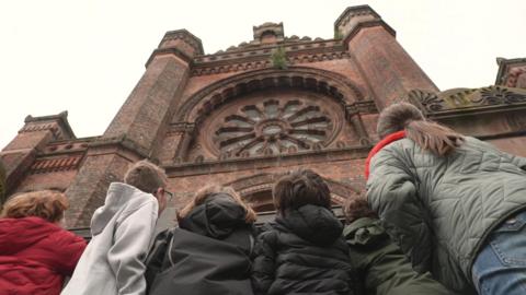 from behind we see children looking up at a stately old building 