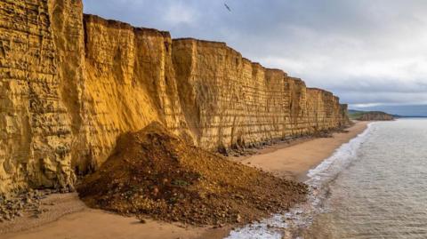 A drone image of a collapsed section of sea cliff which is completely blocking the beach below