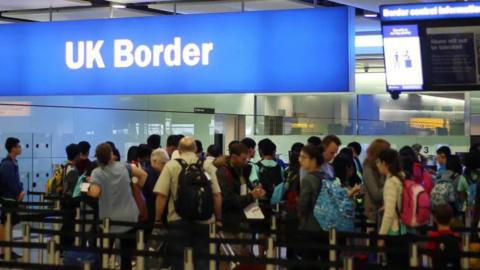 People queue at an airport as they prepare to enter the UK through border control.