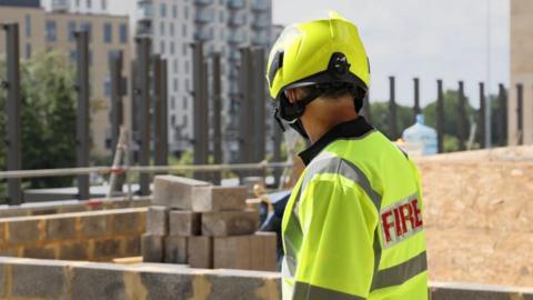 A firefighter wearing a helmet and hi-vis jacket standing by a balcony.