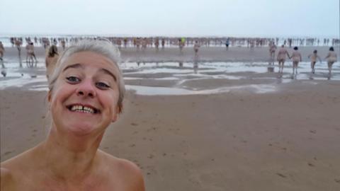 A head-and-shoulders selfie of Jax Higginson, smiling, during one of the North East Skinny Dip events. Behind her are lots of naked people entering the water.