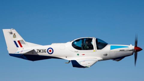 A white RAF Prefect aircraft flying in the blue sky.