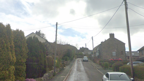 A street view of Station Road with cobbled houses on the right hand side of the road. 