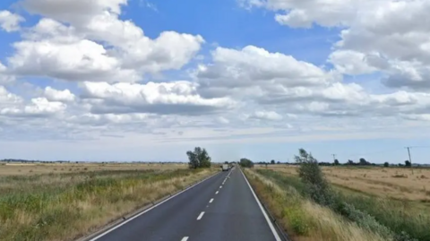 A straight road heads to the horizon with white lines down the middle and flat marshes on either side. 