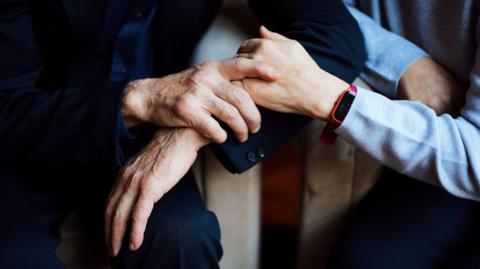 A stock image of a person holding hands with an elderly person. 