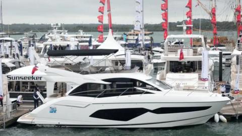 A side-on image of a luxury yacht parked in habour with other yachts behind it. A gazebo behind the yacht on the jetty has the company name 'Sunseeker' written on it. 