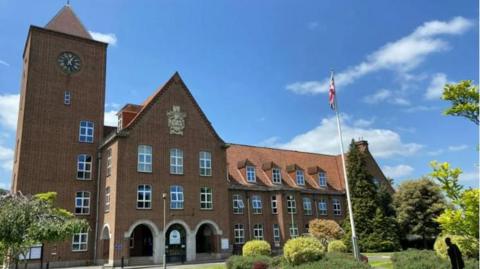 Spelthorne Borough Council offices - a large brick building with a tower at one end, and a union flag flying on a tall flag pole in the grounds